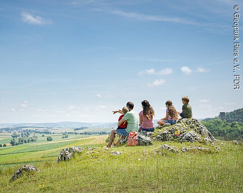 An der Burgruine Niederhaus Eine Gruppe von Menschen sitzt auf einem Hügel und blickt auf eine weite, grüne Landschaft.