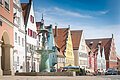 Reichsstraße Donauwörth Straße mit bunten Giebelhäusern und einem Brunnen im Vordergrund. Klarer Himmel im Hintergrund.