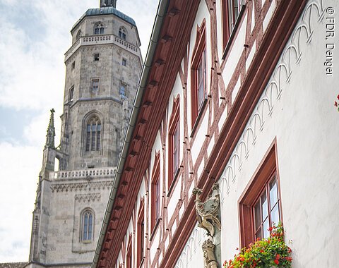 Altstadt Nördlingen mit Blick auf Daniel Fachwerkhaus mit roten Fensterrahmen und Blumenkästen, daneben ein Kirchturm.